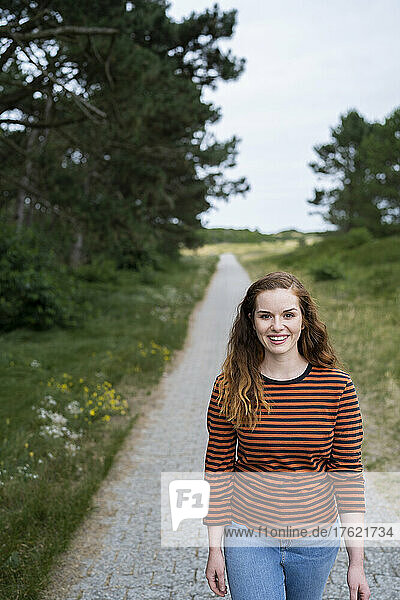 Happy young redhead woman walking on footpath