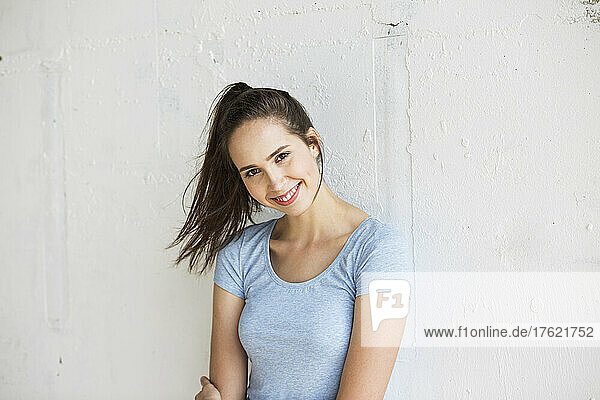Happy woman with ponytail standing in front of wall