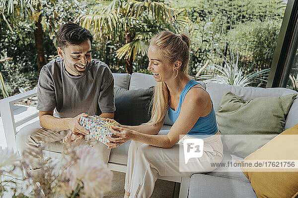 Happy man giving gift to woman sitting at patio