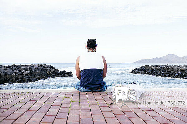 Man sitting on promenade looking at sea