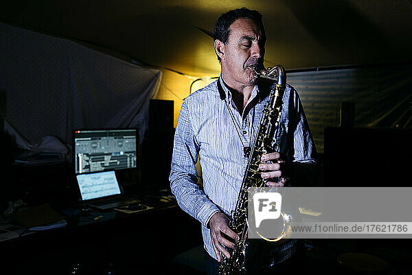 Saxophonist with eyes closed practicing saxophone in recording studio