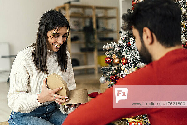 Lächelnde Frau öffnet Geschenk vor ihrem Freund zu Hause