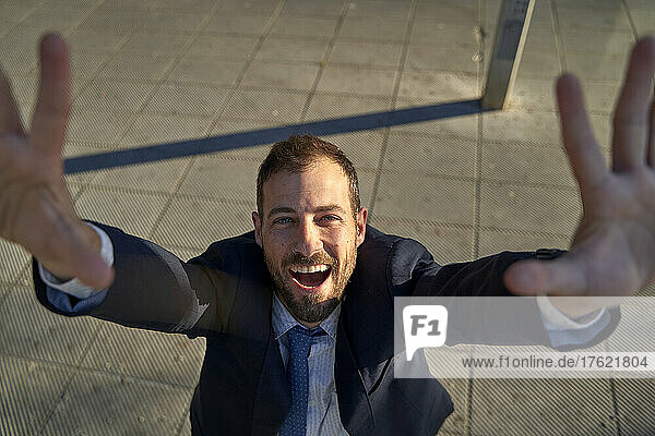 Cheerful businessman with arms raised on footpath