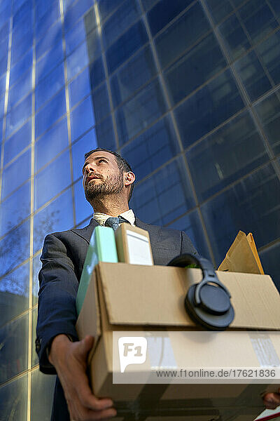 Businessman carrying box of personal belongings by office building