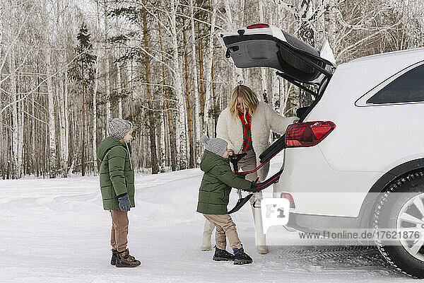 Woman helping son removing toboggan from car trunk win winter forest