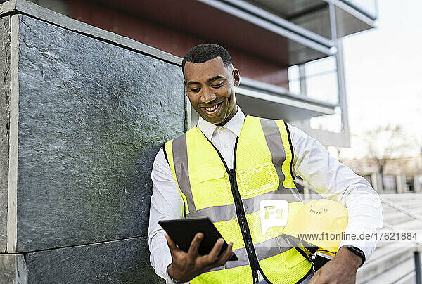 Happy architect with hardhat using tablet PC by wall