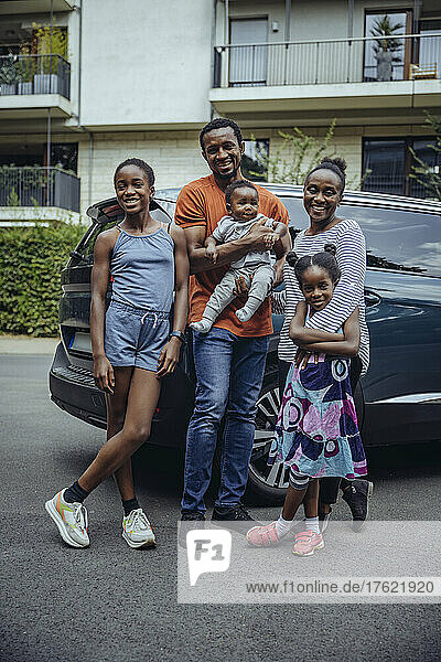 Smiling family standing in front of car on road