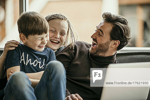 Cheerful father and sons sitting with laptop laughing at home