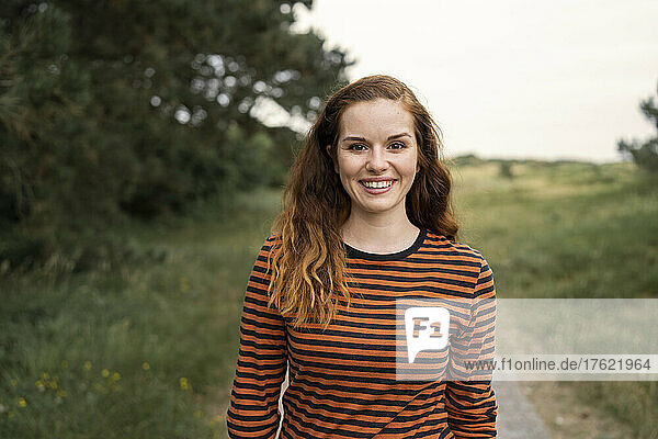 Happy redhead woman wearing striped top standing in meadow