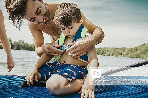 Father fastening life jacket for son in lake