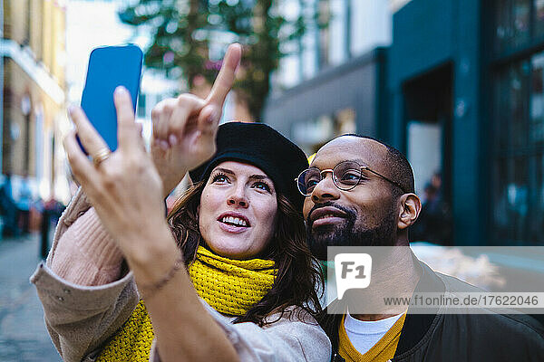 Woman pointing and taking selfie with man on smart phone