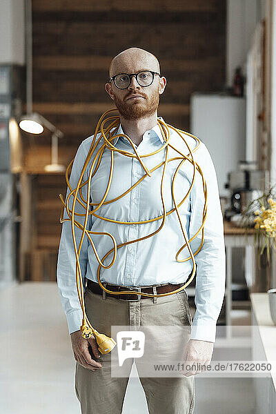 Young businessman covered with cable standing in office