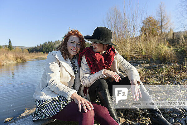 Lächelnde Frau schaut einen Freund an  der an einem sonnigen Tag am Flussufer sitzt