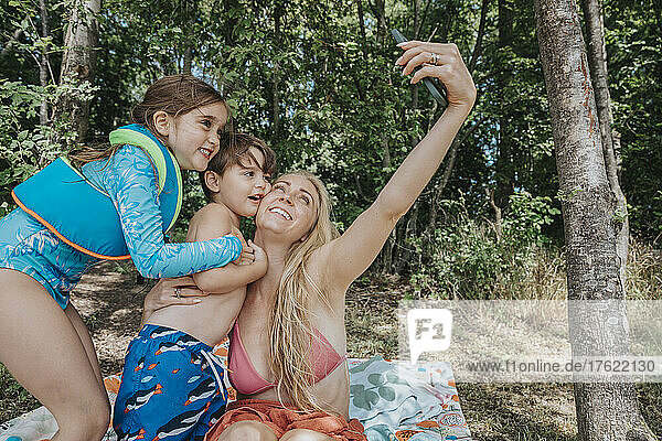 Smiling mother taking selfie with children through smart phone at lakeshore