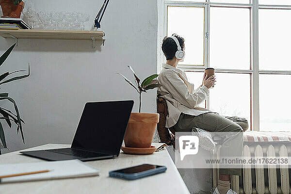 Woman with headphones listening to music by window