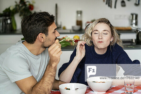 Young man looking at girlfriend eating food with eyes closed siting at table
