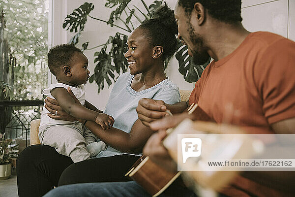 Glückliche Mutter mit Sohn  der zu Hause neben dem Vater sitzt und Gitarre spielt
