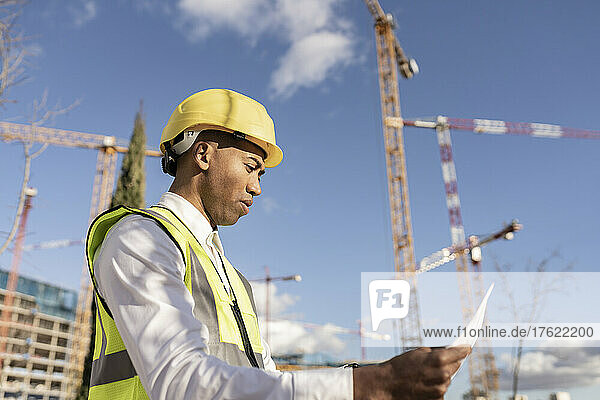 Engineer reading blueprint at construction site on sunny day