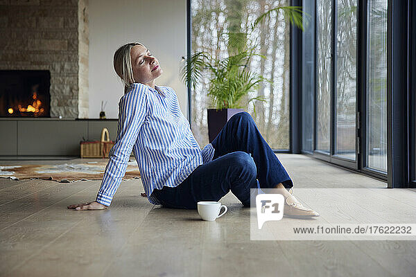 Blond woman with eyes closed siting on floor at home