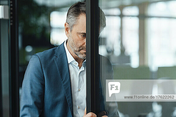 Businessman leaning head on glass door at work place