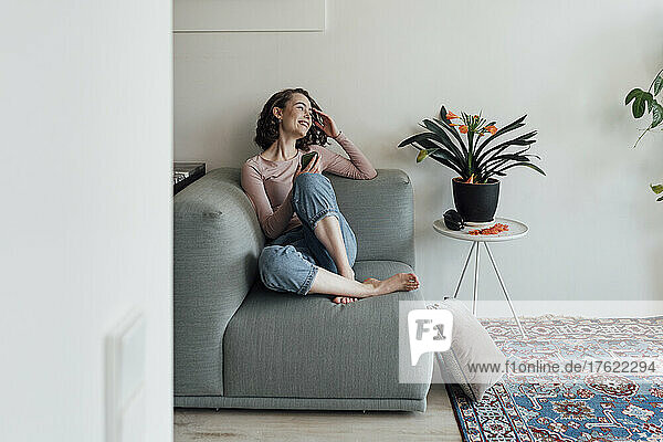 Glückliche Frau sitzt zu Hause mit Smartphone auf dem Sofa