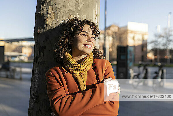Smiling woman leaning on tree trunk