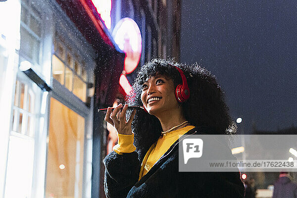 Happy woman talking on mobile phone through speaker in city at night