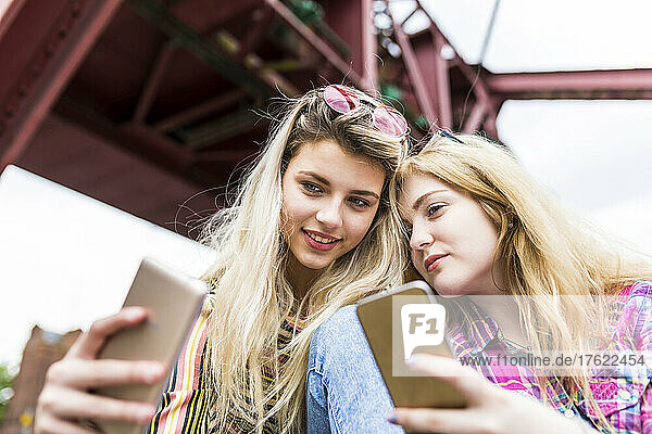 Smiling teenager taking selfie with friend through mobile phone