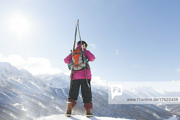 Man with backpack and ski looking at mountain standing on snow in winter