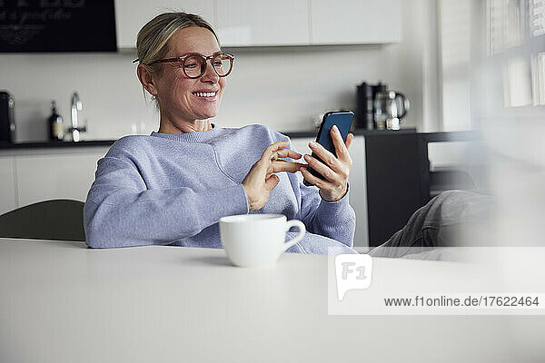 Happy businesswoman using smart phone sitting at table
