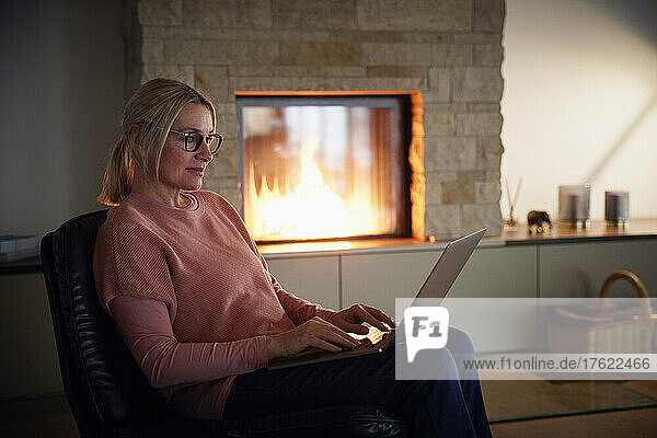 Woman wearing eyeglasses using laptop sitting on chair at home