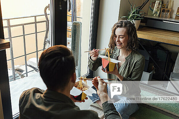 Cheerful woman eating noodles with boyfriend at home
