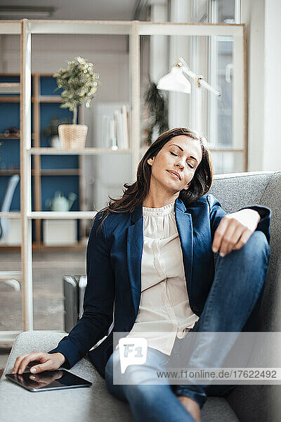 Businesswoman with eyes closed sitting on sofa in office