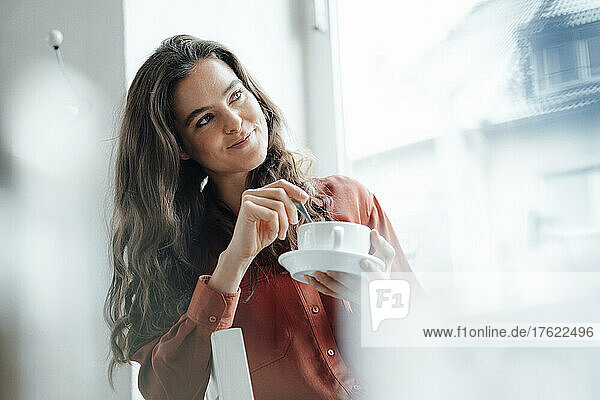 Smiling woman mixing coffee and day dreaming in cafe