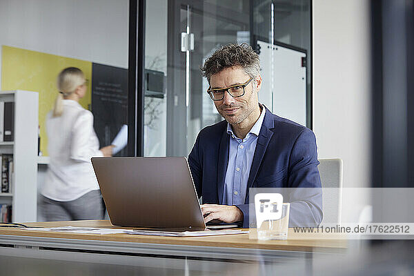 Businessman wearing eyeglasses working on laptop at desk in office