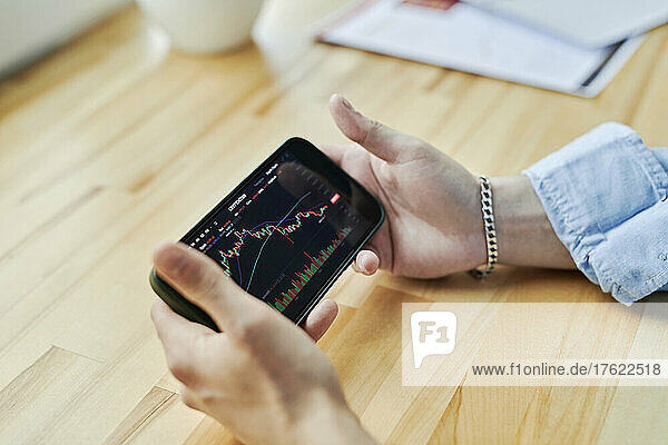 Businessman holding smart phone on desk with cryptocurrency trading graph at office