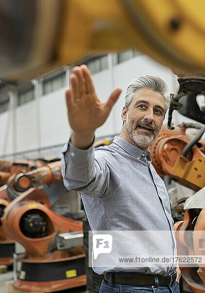 Engineer with gray hair showing machine standing in factory