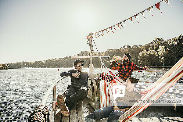 Happy friends enjoying beer sitting on boat bow
