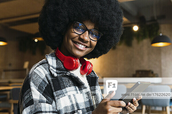 Smiling businesswoman with headphones holding tablet PC in coffee shop