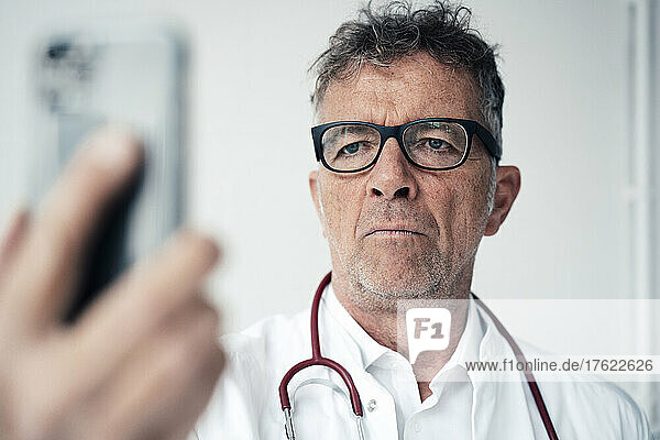 Serious doctor using smart phone in front of wall