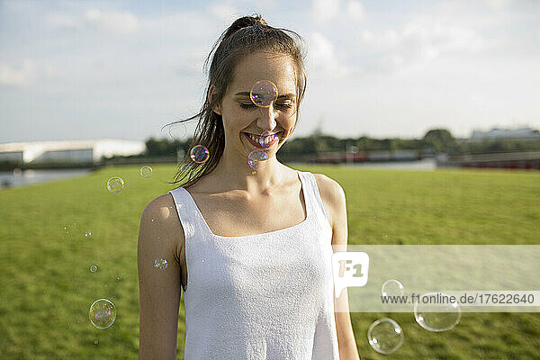 Happy young woman with soap bubbles on meadow