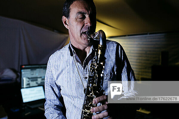 Musician with eyes closed blowing saxophone practicing in recording studio