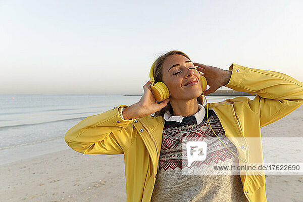 Happy woman with eyes closed enjoying music at beach