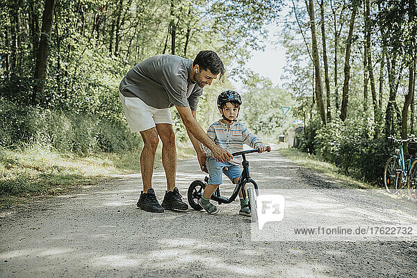 Father teaching son to ride cycle on road