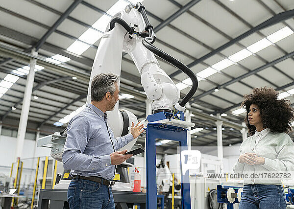 Engineer having discussion about robotic arm in factory