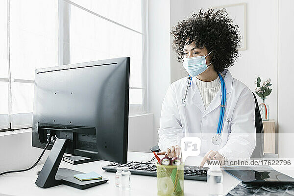 Arzt mit Schutzmaske und Desktop-PC in der medizinischen Klinik