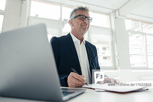 Smiling businessman with laptop and documents on desk in office