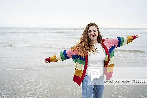 Happy young woman with arms stretched standing at beach