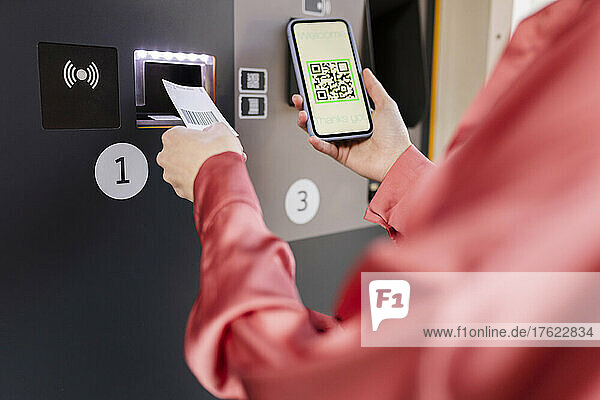 Frau scannt QR-Code am Fahrkartenautomaten per Smartphone am Bahnhof
