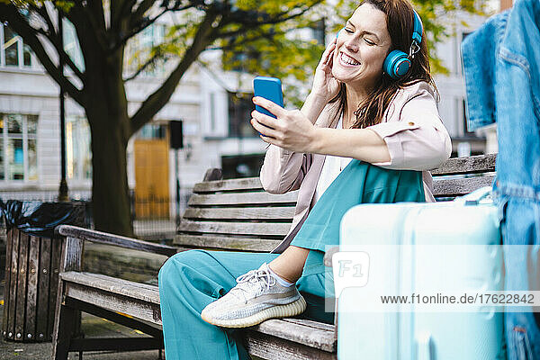 Smiling woman listening music and using smart phone on bench